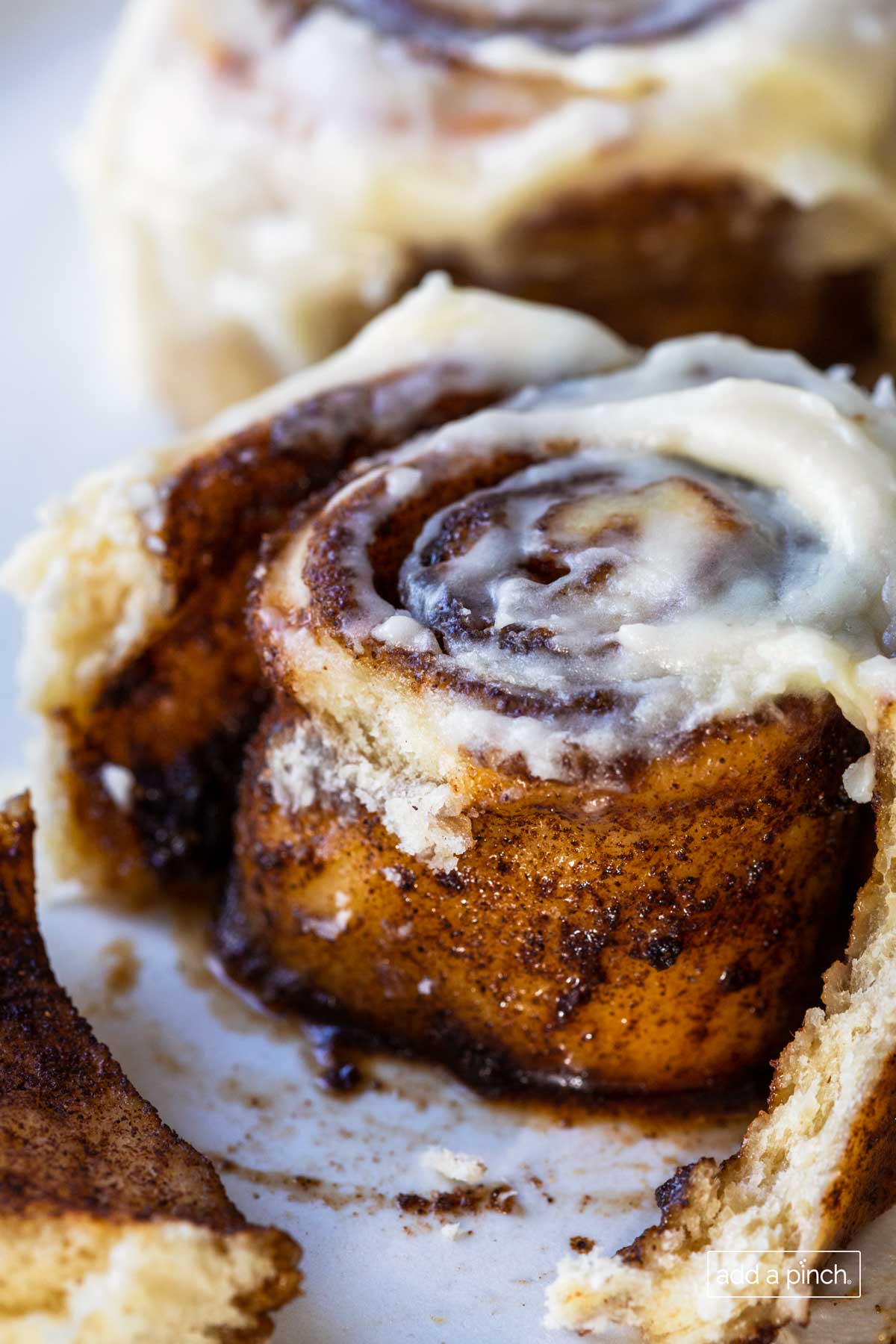 Closeup photo of freshly baked and frosted cinnamon roll with cinnamon filling that's been pulled apart slightly to show the inside. 