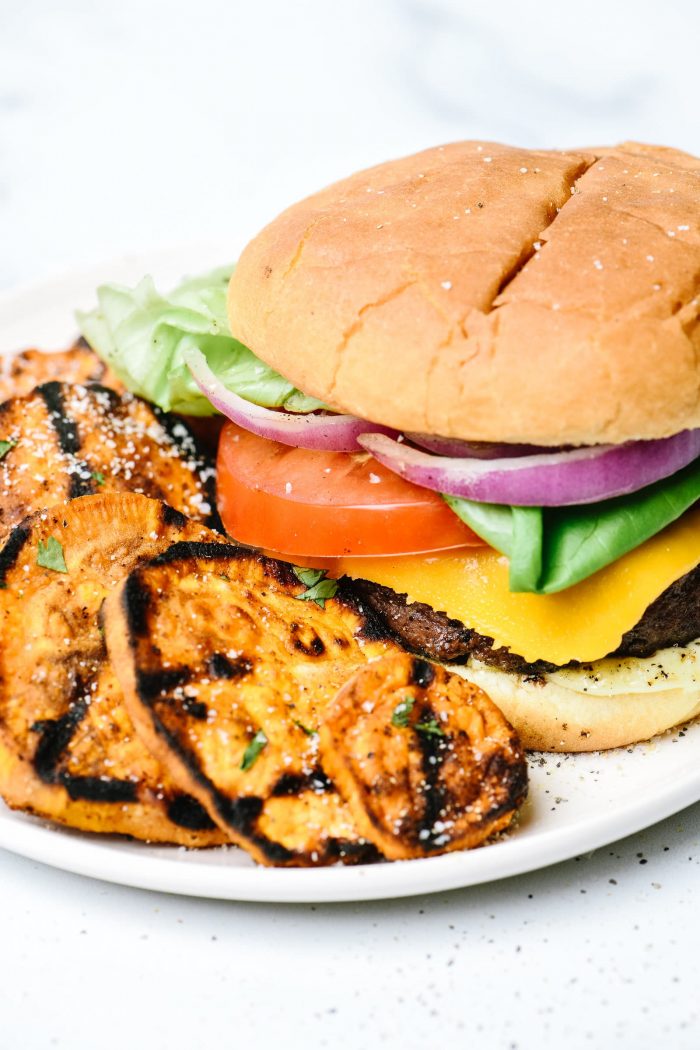 Hamburger on bun with cheese, sliced tomato, red onion, lettuce and side of grilled sweet potatoes on white plate // addapinch.com