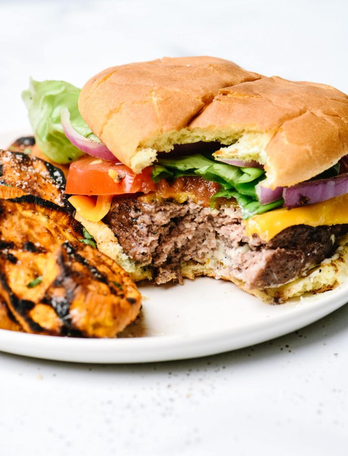 Hamburger on bun and all toppings with bite out of it, with side of grilled sweet potatoes // addapinch.com