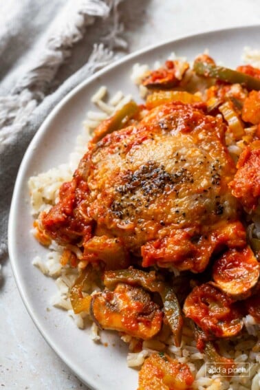 Photo of chicken cacciatore with chicken, peppers, and mushrooms on rice on a white plate.