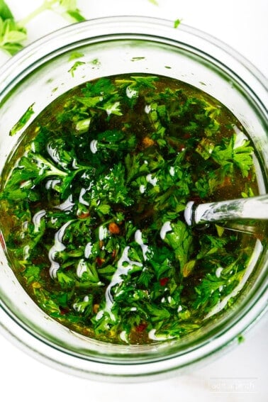 Fresh chimichurri sauce in a glass bowl with a spoon.