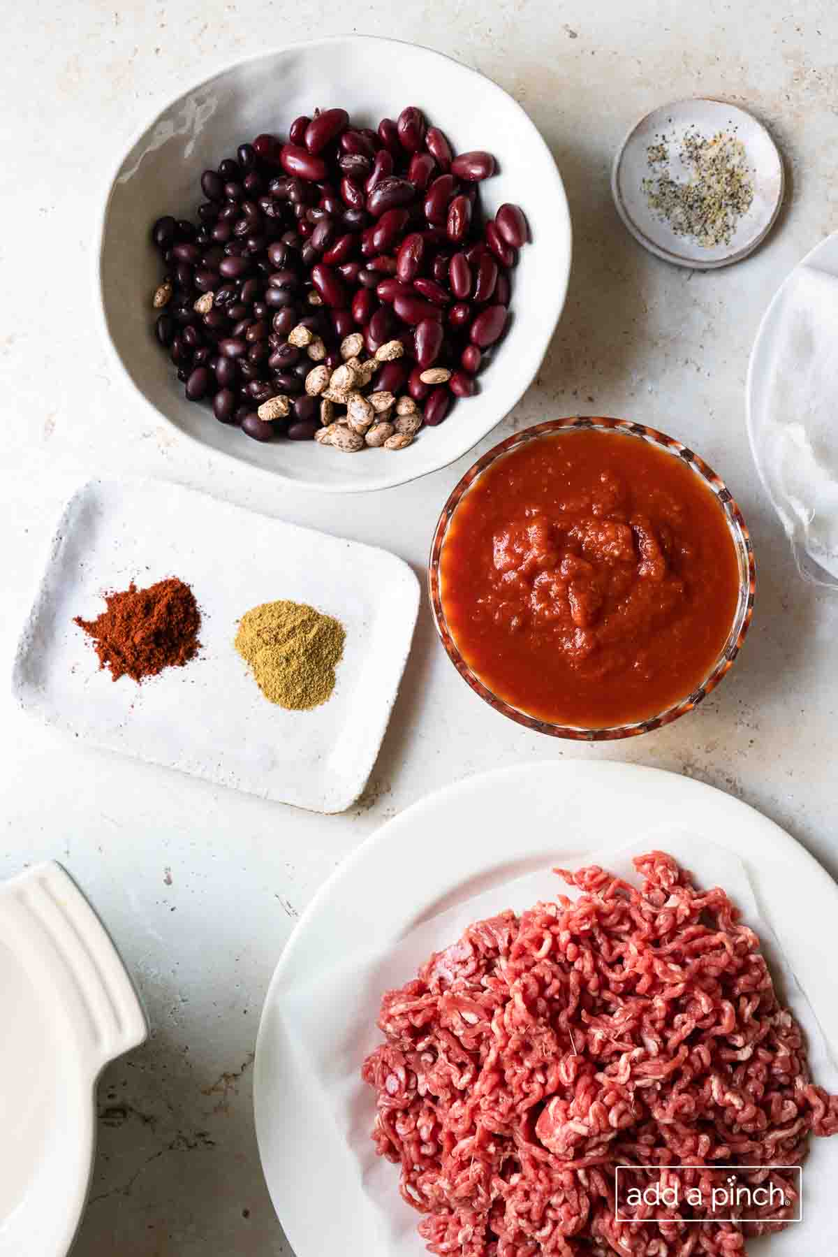 Ground beef, tomatoes, beans, and spices are the ingredients for the best chili recipe. Photographed on a white surface. 
