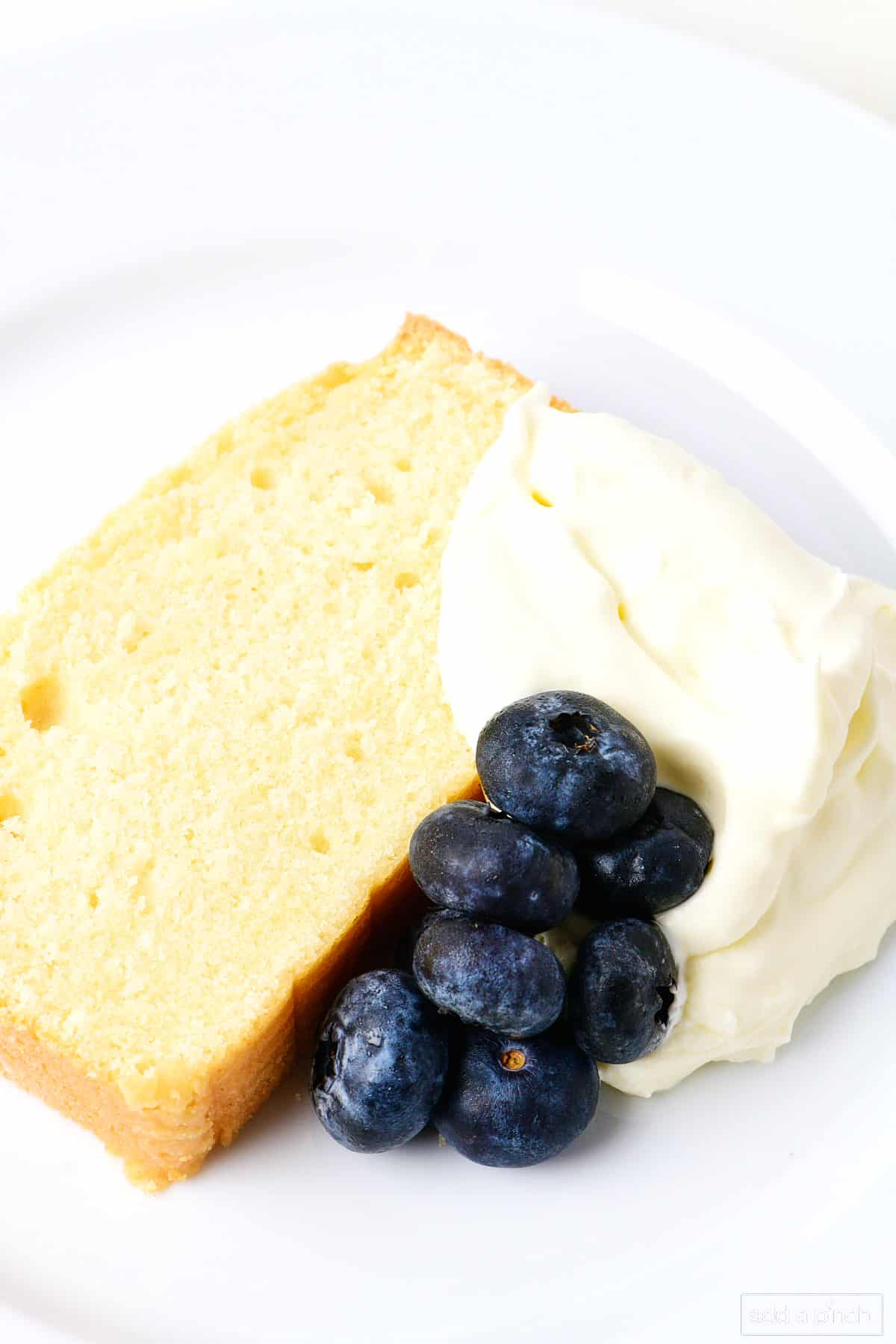 Closeup picture of pound cake slice garnished with homemade whipped cream and blueberries. 