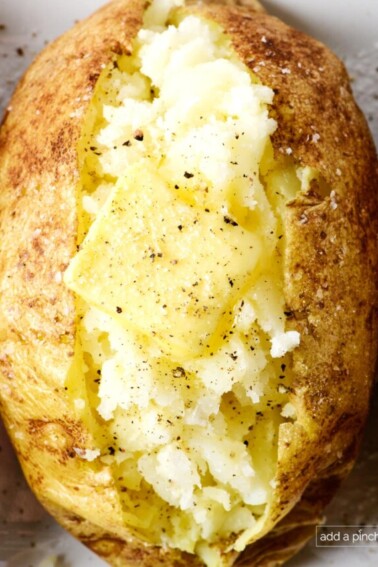 Baked potato with butter, salt and pepper on a white platter.