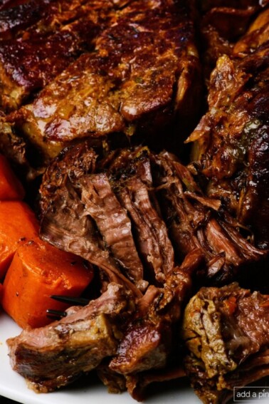 Pot roast surrounded by fresh vegetables and herbs.