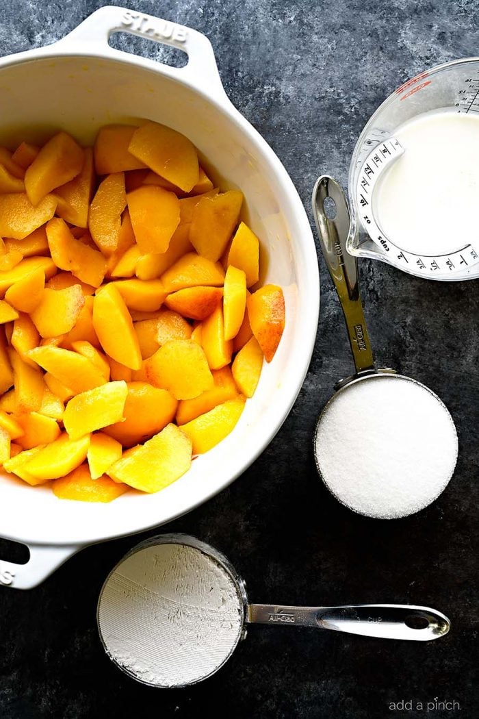 Overhead photograph of sliced fresh juicy peaches in a white bowl with filled measuring cups on a stone countertop. // addapinch.com