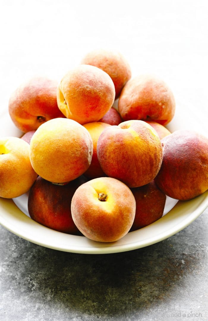 White bowl filled with fresh peaches on a stone countertop. // addapinch.com
