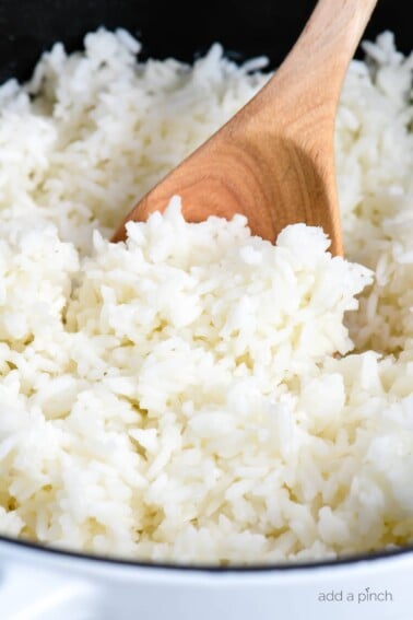 Fluffy white rice in a white Dutch oven with a wooden spoon. // addapinch.com