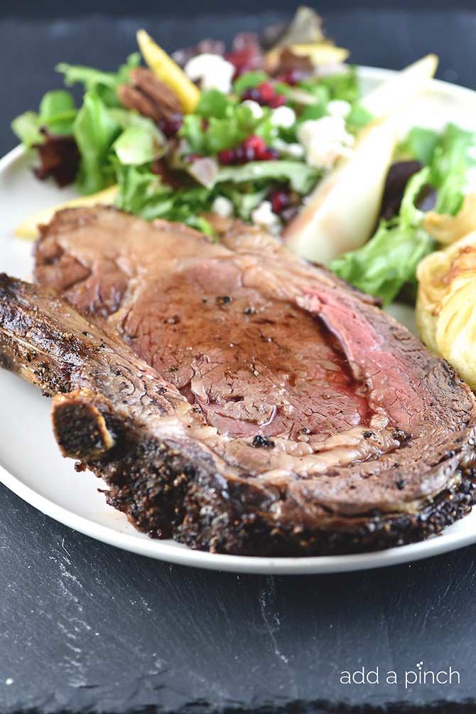 Juicy slice of prime rib surrounded by a colorful salad on white tray placed on a stone counter.