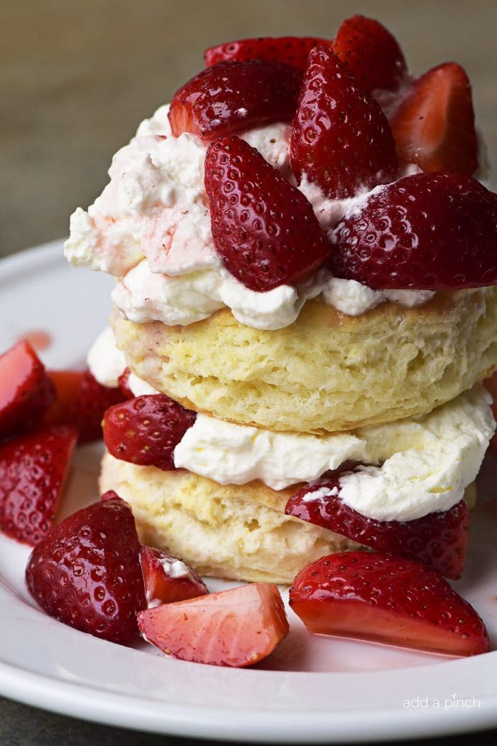 White plate served with Strawberry Shortcake with whipped cream in between and atop the biscuits along with ripe strawberry slices // addapinch.com