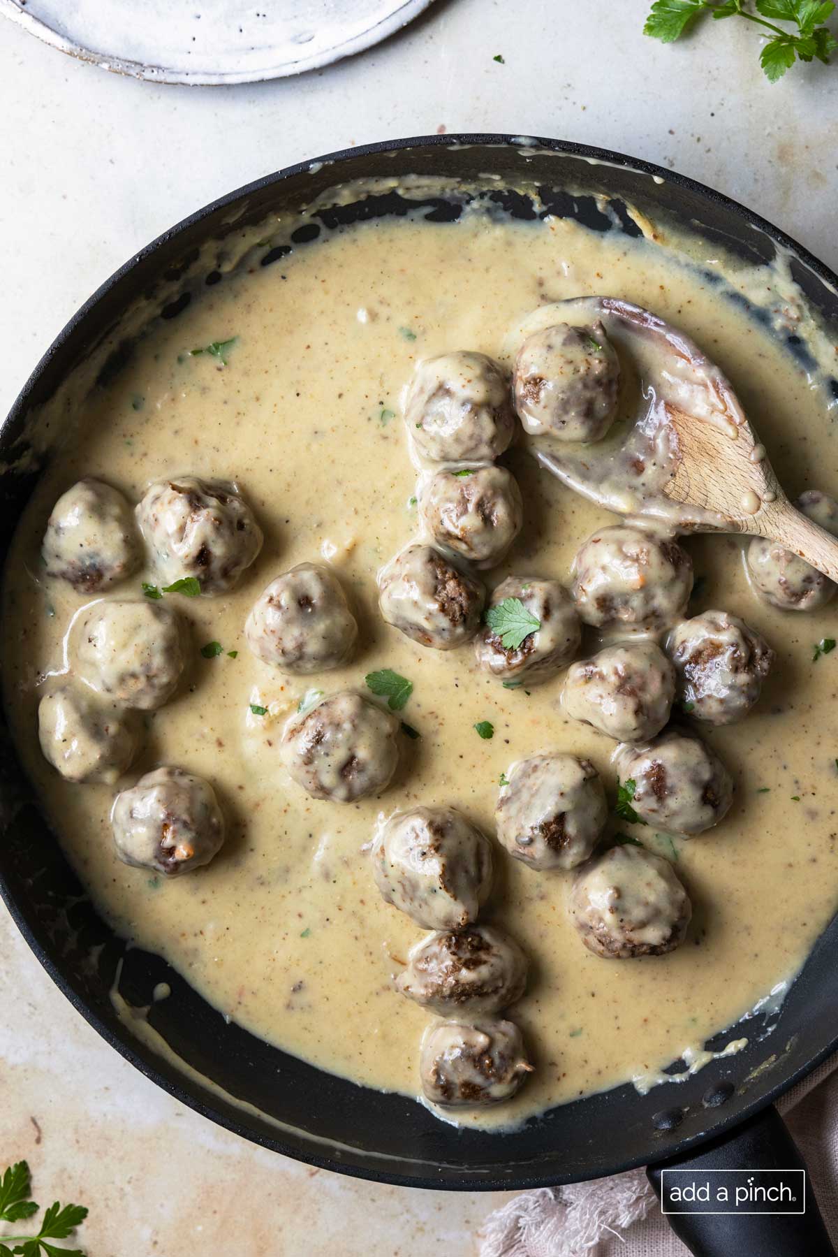 Photo of Swedish Meatballs in rich, creamy sauce in a skillet with a wooden spoon.