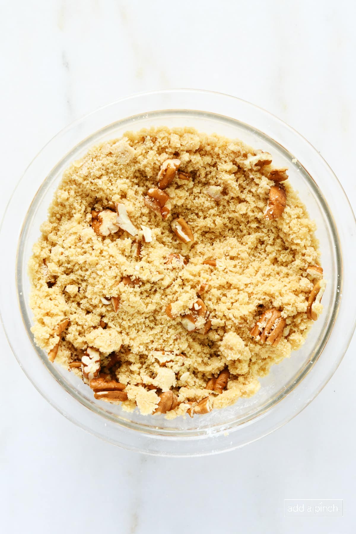Crumble topping with pecans in a glass bowl.